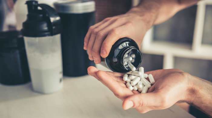 A man pouring BCCA supplement capsules from a bottle into his hand